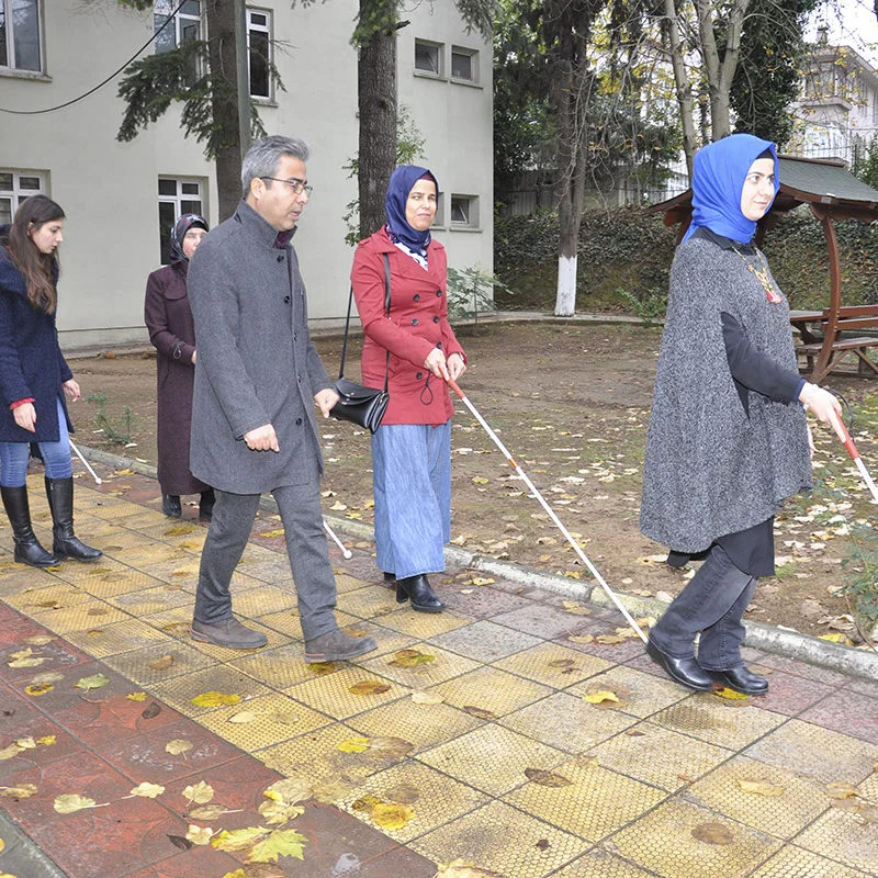 Fotoğrafta Rehabilitasyon Merkezi bahçesinde bağımsız hareket eğitimi alan 2 görme engelli ve 2 eğitimci  yer alıyor.